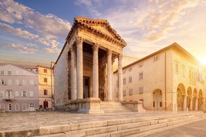 Un ancien temple grec, doté de colonnes, situé sur une place bordée de bâtiments modernes.
