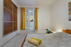 A bedroom with a bed, a window with curtains, a plant, and a wall-mounted artwork.