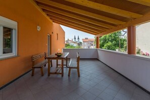 A balcony with a wooden table and two chairs, a window, and a view of buildings in the background.