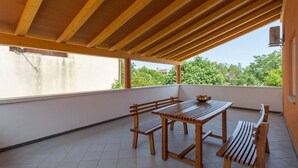 A covered outdoor patio with a wooden table and benches, a view of greenery, and a tiled floor. - Apartment with pool in Medulin A3 (Medulin)