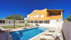 Una casa moderna con piscina, sillas de descanso y un porche cubierto.