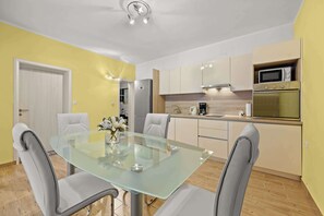A modern kitchen with a glass dining table, grey chairs, and a microwave.