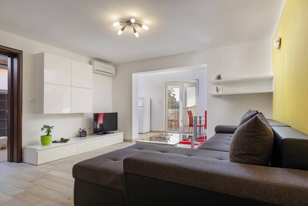 Ein modernes Wohnzimmer mit grauem Sofa, einem Flachbildfernseher, einer weißen Kommode und einer gelben Akzentwand.