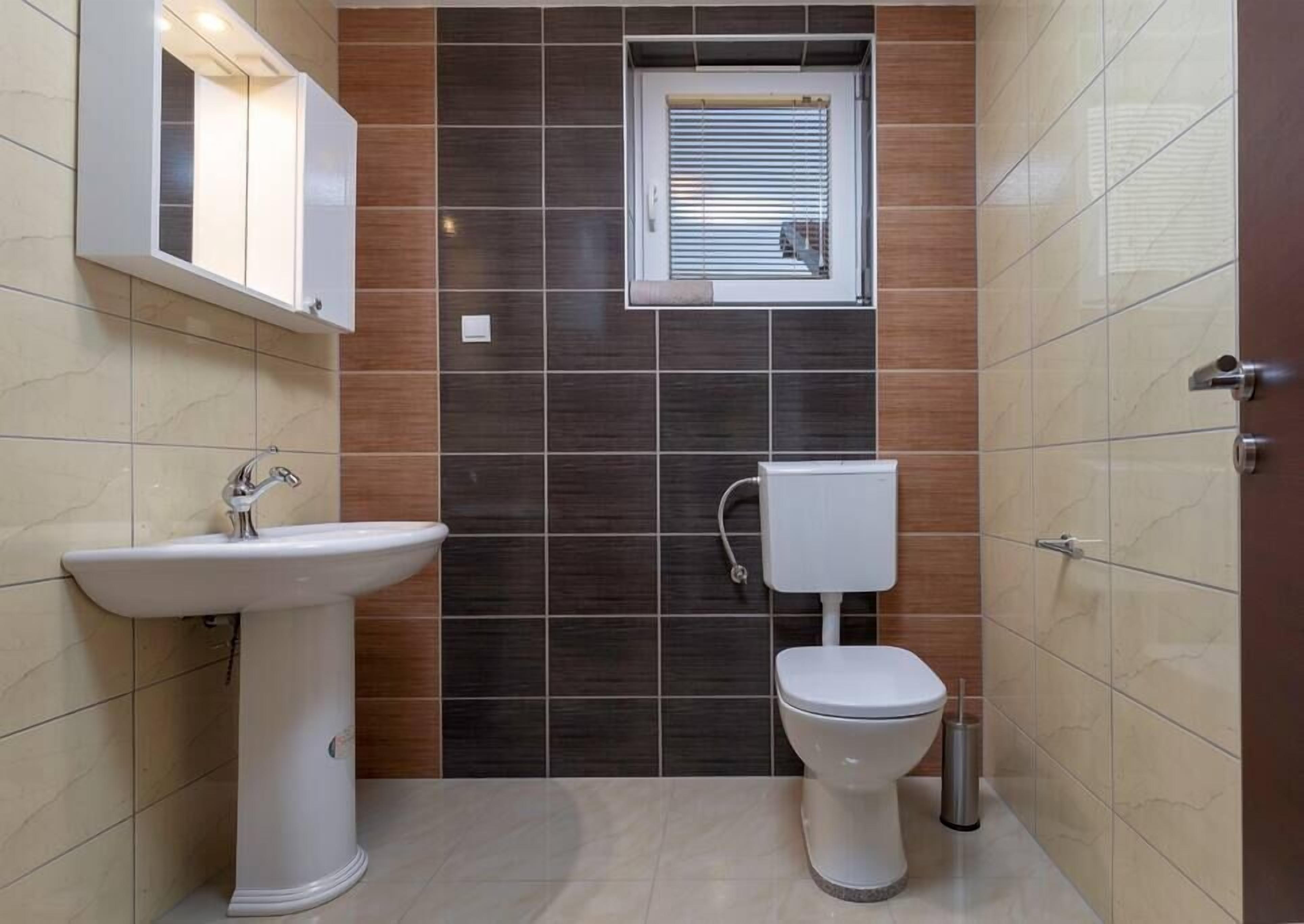 Een badkamer met een wastafel op voetstuk, een toilet, een raam en een spiegel.