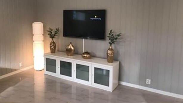 A modern living room with a flat-screen TV mounted on the wall, a white entertainment unit with decorative items, and a floor lamp. - Notodden Sentrum Apartment NO 3 (Notodden)