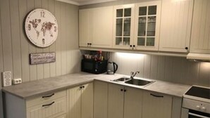 A kitchen with white cabinets, a world map clock, a microwave, a sink, and an oven. - Notodden Sentrum Apartment NO 3 (Notodden)