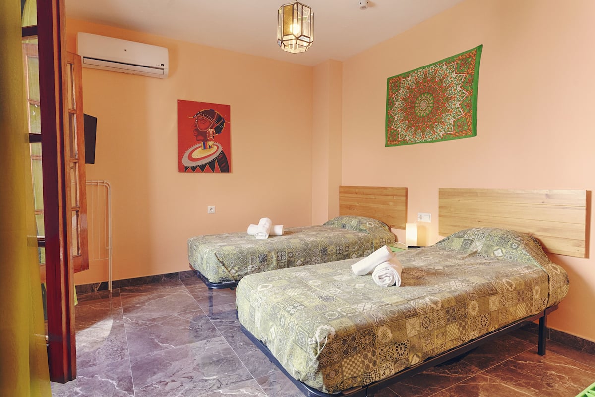 Une chambre d’hôtel avec deux lits simples, une tête de lit en bois, une tapisserie et un appareil de climatisation.