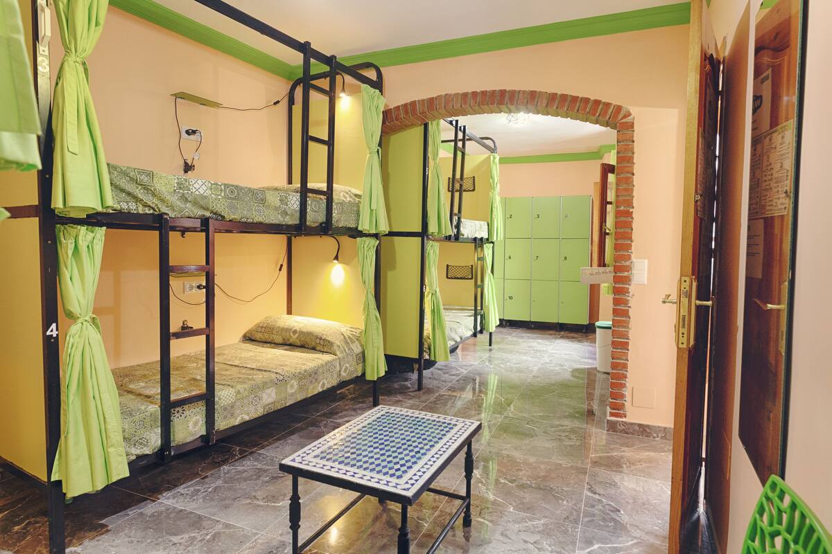 Une chambre avec des lits superposés, une petite table et un rideau vert.