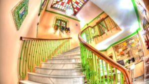 Una escalera de caracol con barandas verdes y un pasamanos de madera, que conduce a una habitación con un escritorio y una silla.