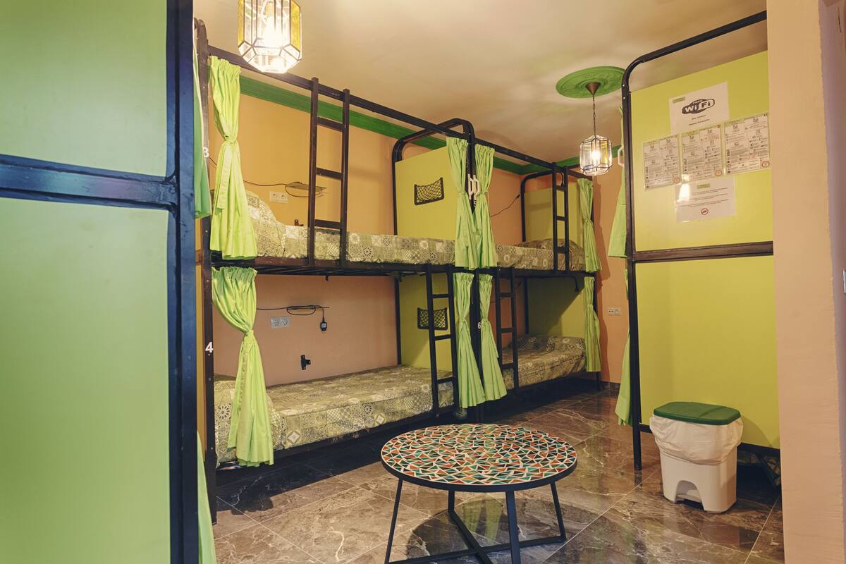 Une chambre de dortoir avec des lits superposés, une petite table ronde et une poubelle.