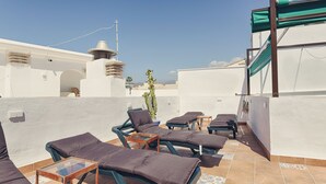 Una terraza en la azotea con sillones de sol, una mesita y una planta en maceta.