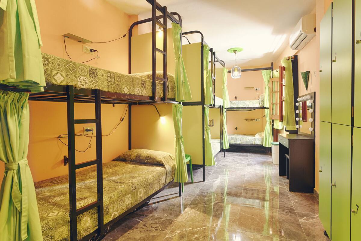 Une chambre de dortoir avec des lits superposés, une petite kitchenette et une coiffeuse avec des miroirs.