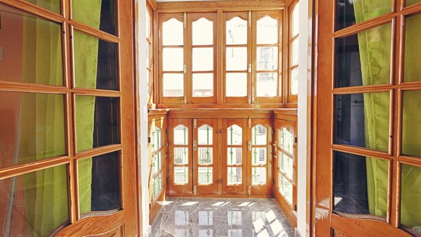 Una habitación con ventanas de madera grandes y cortinas verdes.