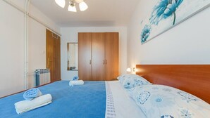 Une chambre à coucher avec un lit, une armoire en bois, une salle de bain avec un porte-serviettes et un tableau accroché au mur.