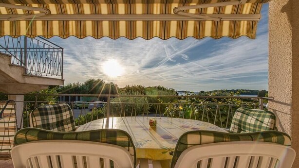 An outdoor patio with a round table and chairs, a view of the landscape, and a railing.