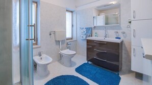 A modern bathroom with a glass shower enclosure, a bidet, a toilet, a vanity with a mirror, and a blue rug.