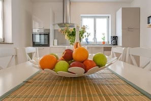 A kitchen with white cabinets, a stainless steel oven, a glass vase with flowers, and a fruit bowl on the table. - Villa Tanga near Rovinj for 8 persons with pool (Rovinj)