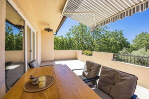 A patio with a wooden table and chairs, a hanging light fixture, and a view of trees and a balcony railing. - Holiday Home with pool and garden - Tervis (Trviž)