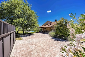 A paved patio area with a house in the background, surrounded by greenery and trees. - Holiday Home with pool and garden - Tervis (Trviž)