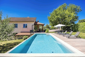 A rectangular swimming pool with a tiled deck, a stone wall, and a house with a tiled roof. - Holiday Home with pool and garden - Tervis (Trviž)