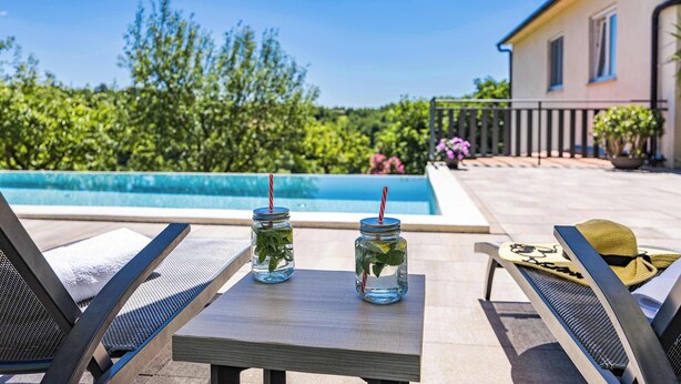 A poolside area with two glass jars containing drinks, a lounge chair, and a small table.