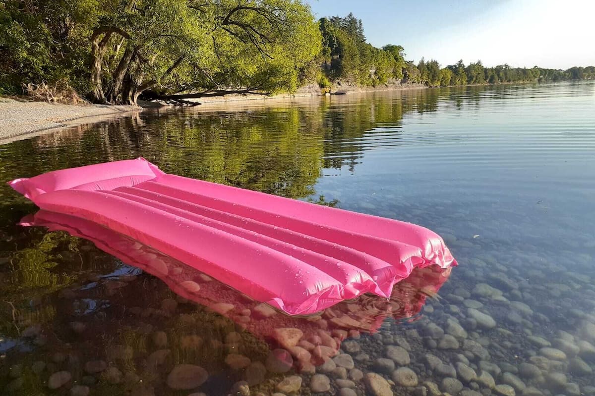 A pink inflatable raft on a clear river with visible rocks and trees in the background.