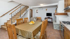 Un comedor con una mesa y sillas de madera, una escalera, una cocina con estufa y un televisor.