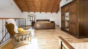 Ein Schlafzimmer mit Holzbalkendecke, einem Bett, einem Kleiderschrank und einem Sessel.