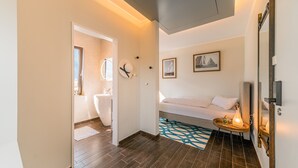 A hotel room with a bed, a bedside table with a lamp, a wall-mounted clock, and a framed picture.