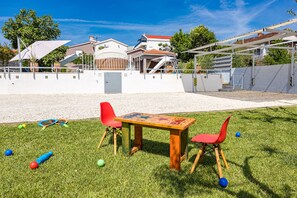 A grassy outdoor area with a wooden table and two red chairs, surrounded by a white wall and a covered walkway. - Five bedroom villa Emily with pool in Medulin (Medulin)