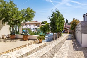 A paved pathway lined with potted plants, leading to a building with a tiled roof and a visible slide. - Five bedroom villa Emily with pool in Medulin (Medulin)
