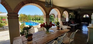 Une terrasse couverte avec une piscine, une table en bois, des plantes en pot et des meubles d’extérieur.