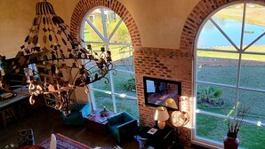Una habitación con chimenea de ladrillo, ventanas arqueadas grandes, un candelabro y un televisor.