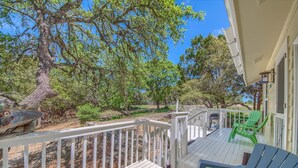 A wooden deck with white railings, green chairs, and a large tree in the background.