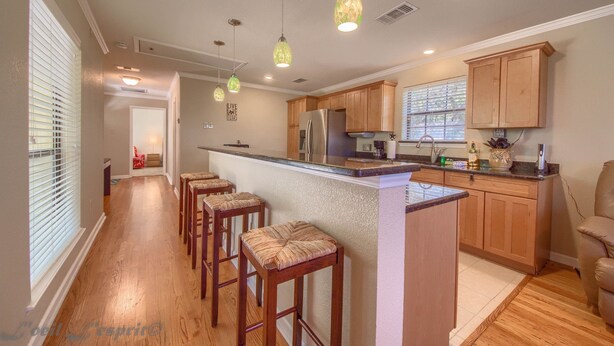 A kitchen with wooden cabinets, a central island with stools, pendant lighting, and a refrigerator.