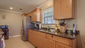 A kitchen with wooden cabinets, a stainless steel refrigerator, a sink, and a window with blinds.