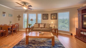 A living room with a ceiling fan, wooden furniture, a sofa, and large windows with blinds.