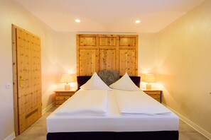 A neatly made bed with white linens, two bedside lamps, a wooden headboard, and a wooden door.