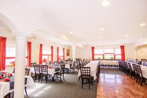 A large dining hall with multiple tables and chairs, arranged in rows.