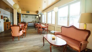 A spacious living area with a wooden floor, a sofa, dining table, chairs, and large windows.