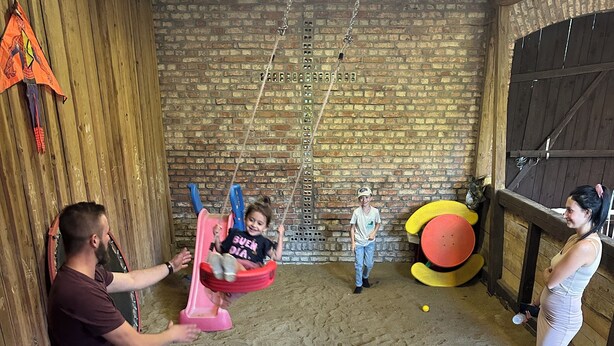 A room with a brick wall, a swing set, a small inflatable pool, and a red chair. - Historic holiday home for families and groups
with garden and play barn. (Janowice Wielkie)