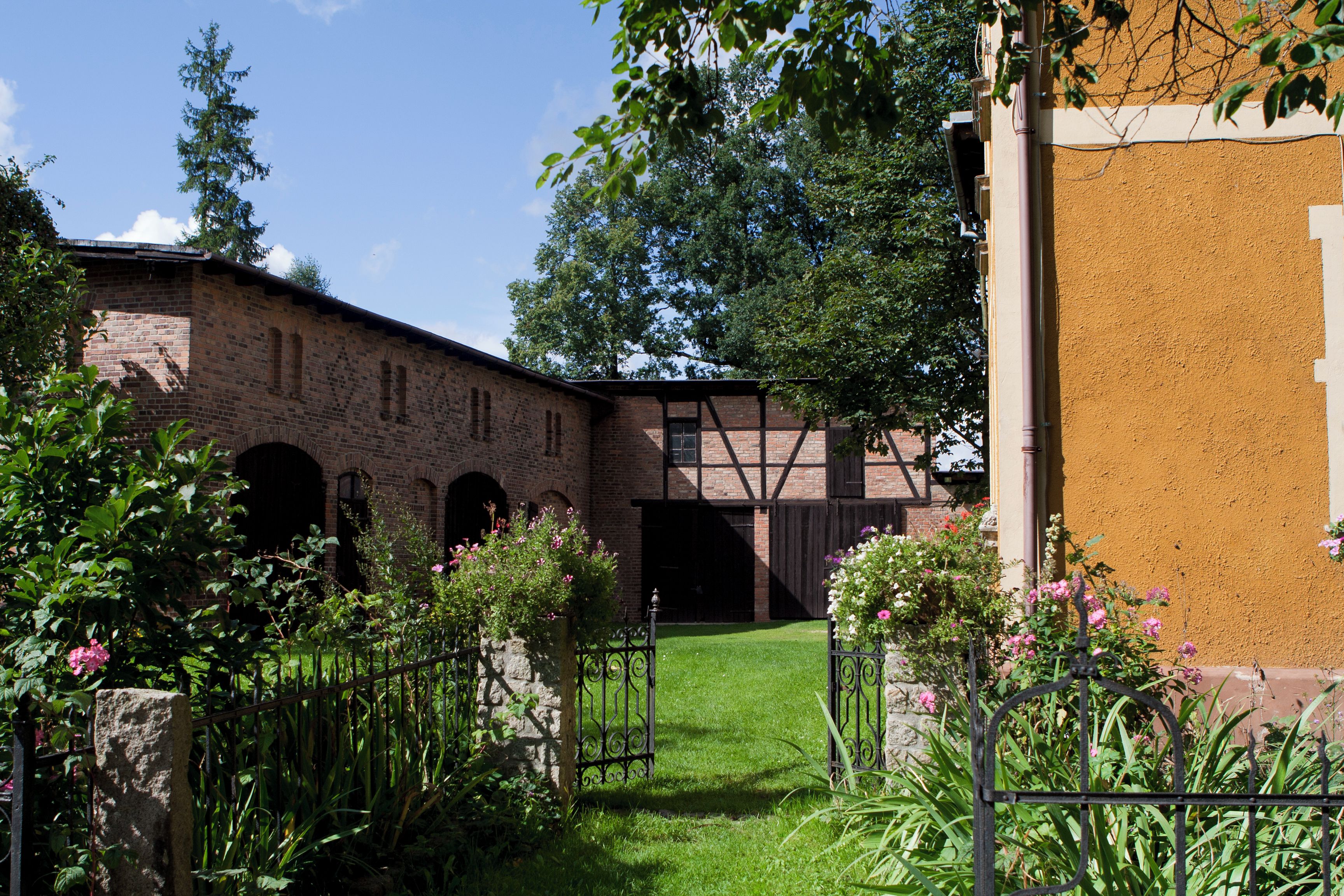 A courtyard with a brick building, a wooden bridge, and a grassy area with flowers.