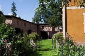 A courtyard with a brick building, a wooden bridge, and a grassy area with flowers. - Historic holiday home for families and groups
with garden and play barn. (Janowice Wielkie)