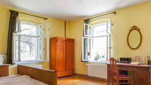A bedroom with a wooden bed, a desk with a chair, and two windows with curtains. - Historic holiday home for families and groups
with garden and play barn. (Janowice Wielkie)