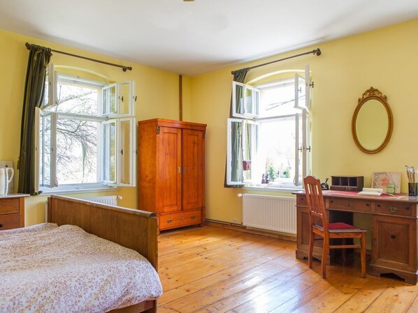 Um quarto com cama de madeira, uma escrivaninha com cadeira e duas janelas com cortinas.