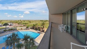 Un balcon avec vue sur une piscine, des palmiers et un paysage lointain.