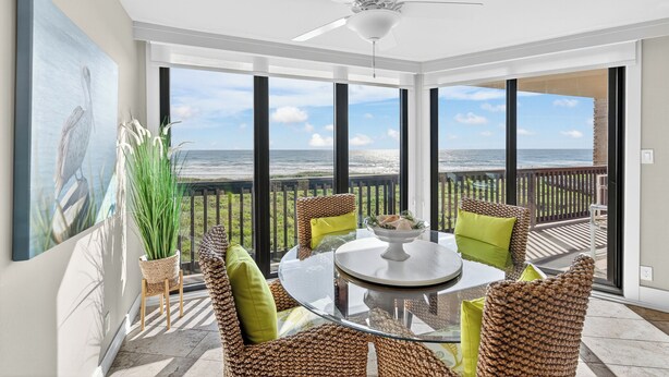 Un balcon avec une table en verre et des chaises en osier, donnant sur une plage.