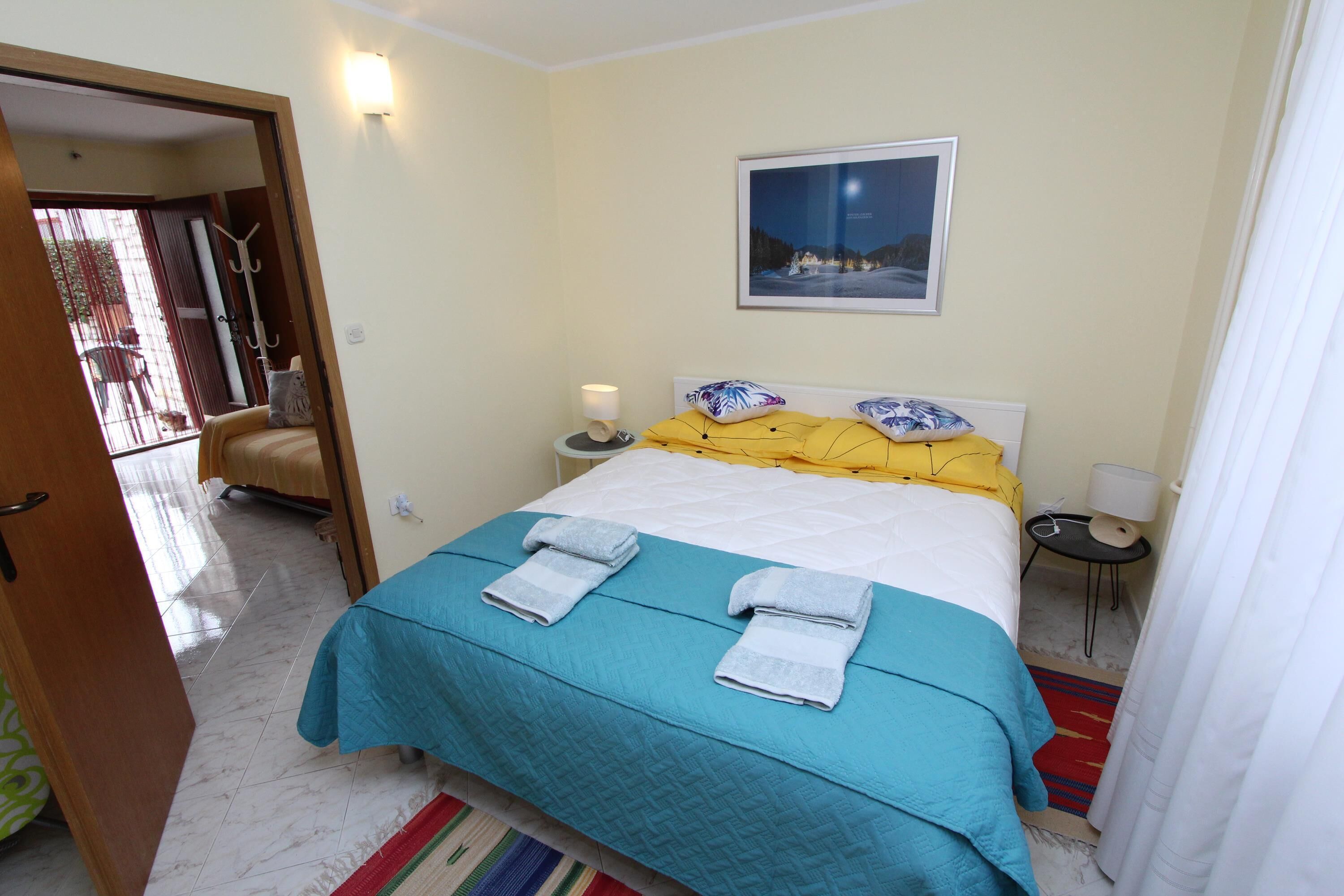 A hotel room with a bed, a bedside table with a lamp, a picture on the wall, and a view of the outside balcony.