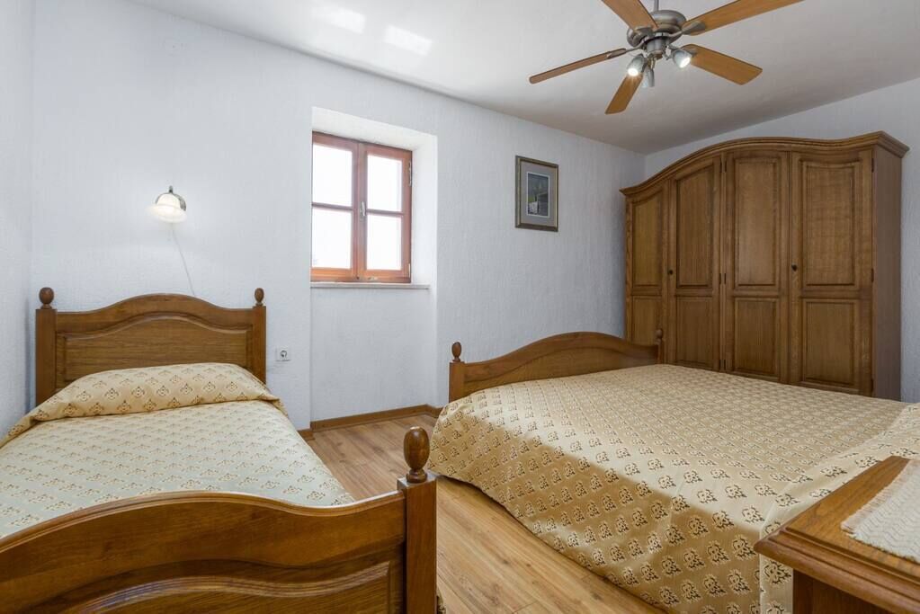 A bedroom with two wooden beds, a ceiling fan, a window, and a wardrobe.