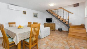 Ein Essbereich mit Tisch, Stühlen und einer Obstschale. Es gibt ein Sofa, einen Fernseher und eine Treppe.
